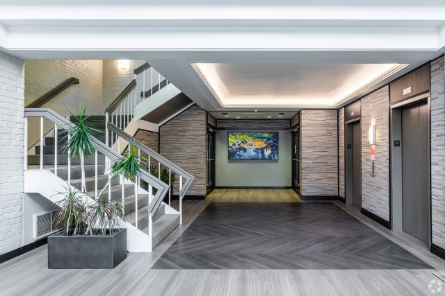 Front view of Atrium West ground floor lobby with large painting on the back wall of a waterfall, white finishes, natural stone, and live plants
