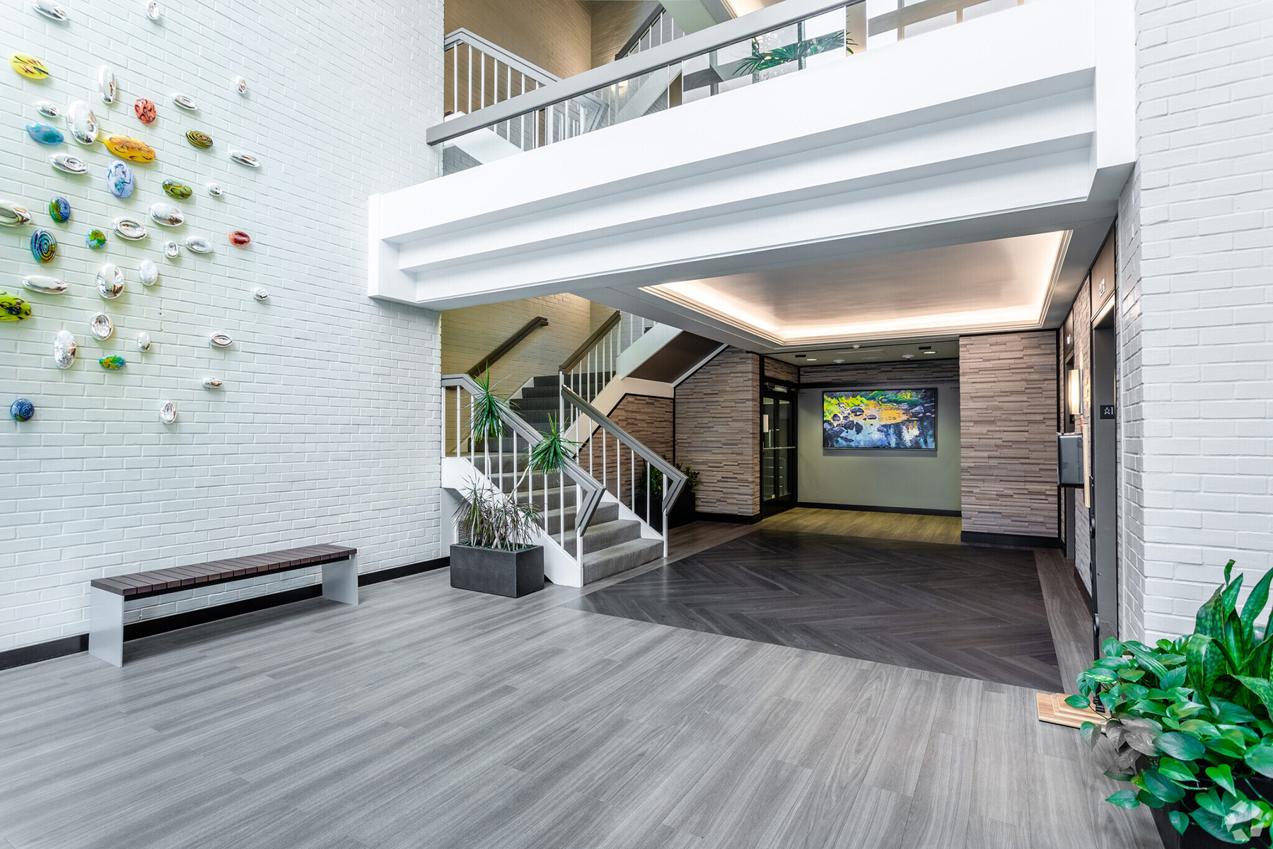Atrium West lobby with bright white surfaces, natural stone finishes, live plants, and paintings and modern glass art on the white painted brick wall